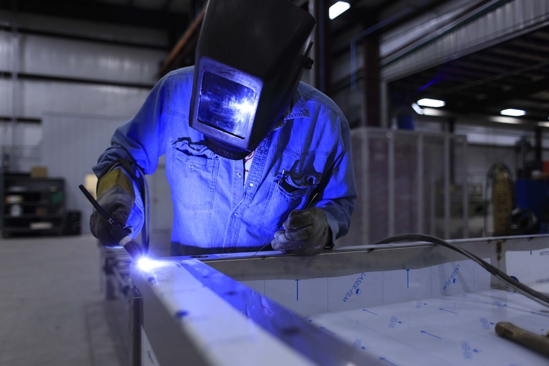 A man in blue coveralls and a welding helmet is welding a piece of metal. Safety first!