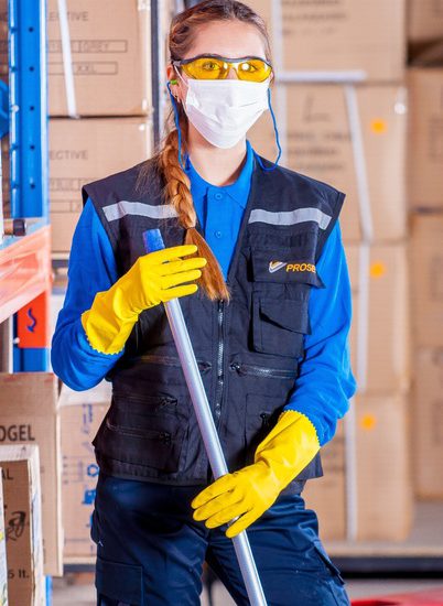 A woman holding a mop or broom wearing safety gear and a medical face mask. Manufacturers should focus on grooming their workforce in 2021.